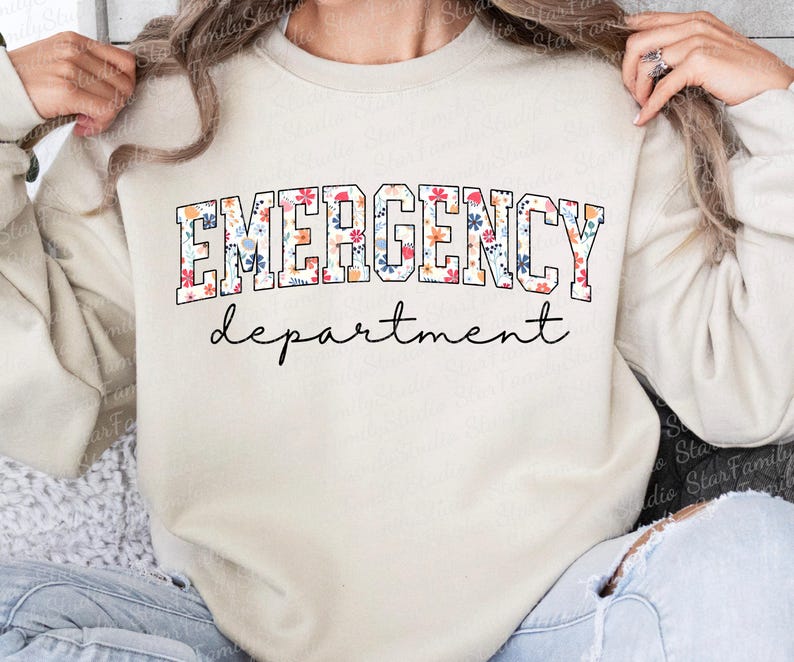 K&ouml;nnte beinhalten: Ein cremefarbener Pullover mit dem Text "EMERGENCY department" in schwarzen Buchstaben mit einem Blumenmuster.