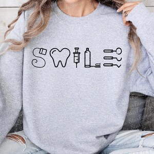 May include: Gray sweatshirt with a black graphic of a tooth, syringe, and dental tools with the word "SWILE" above the graphic.