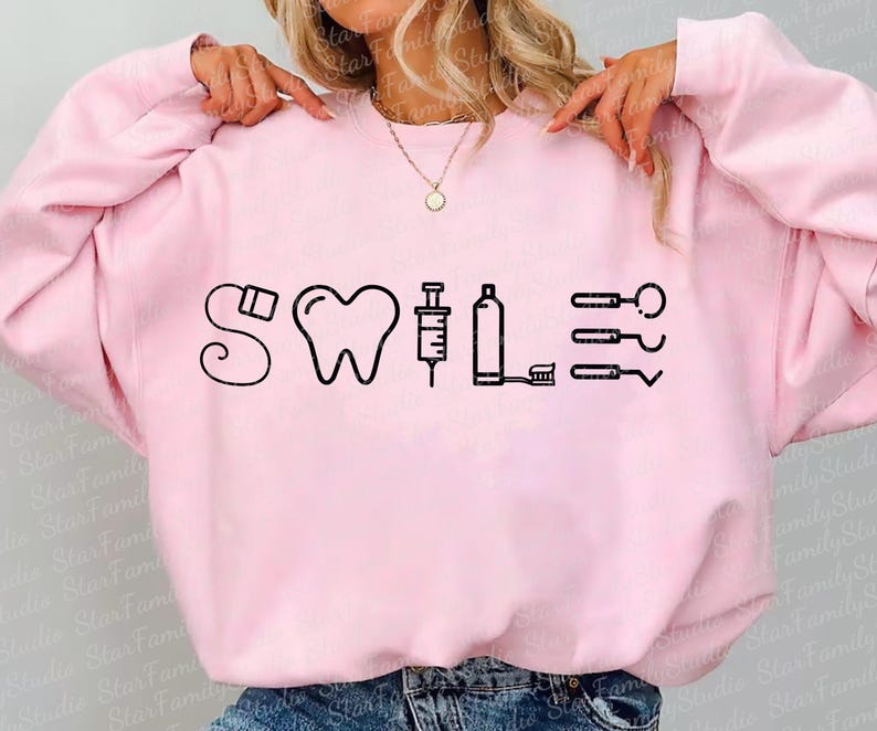 May include: Pink sweatshirt with a black graphic design that says "SWILE" with dental tools and a tooth.
