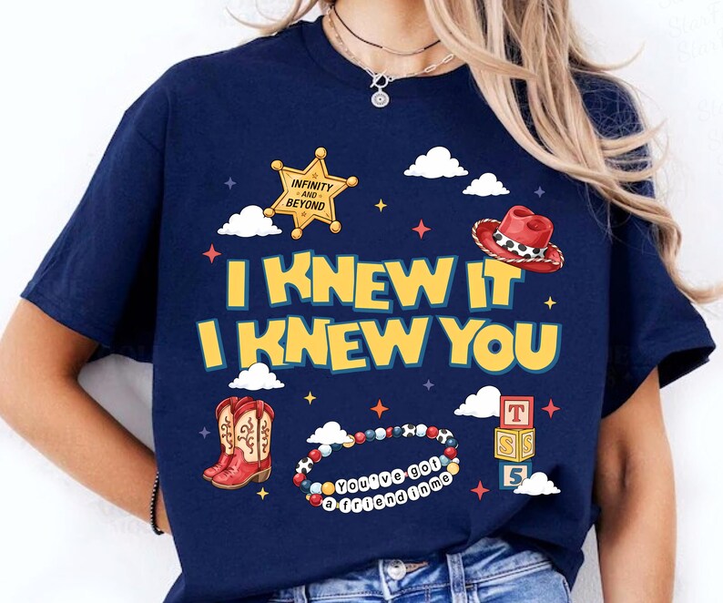 Może przedstawiać: Granatowy t-shirt z ż&oacute;łtym napisem I KNEW IT I KNEW YOU. Grafika zawiera złotą odznakę szeryfa z napisem INFINITY AND BEYOND, czerwony kowbojski kapelusz, brązowe kowbojki, bransoletkę z koralik&oacute;w z napisem YOU'VE GOT A FRIEND IN ME oraz stos trzech klock&oacute;w z literami T, S i 5, otoczonych białymi chmurami i małymi gwiazdkami.