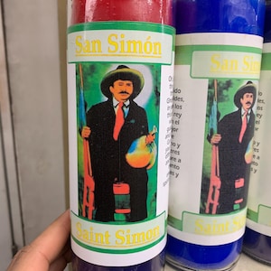 May include: Two red and blue glass candle jars with images of Saint Simon. The red candle jar has a green label with the text "San Simon" and "Saint Simon". The blue candle jar has a green label with the text "San Sin" and "Saint Sin".