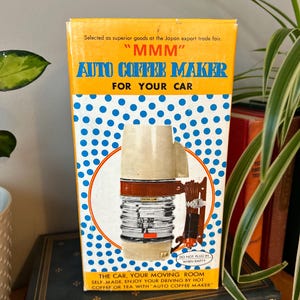 May include: A vintage box for a "MMM" brand car coffee maker. The box is yellow and blue with white polka dots. The box features a picture of the coffee maker, which is silver and white with a brown handle. The text on the box reads "MMM" Auto Coffee Maker for Your Car. The box also includes the text "The Car, Your Moving Room. Self-made, enjoy your driving by hot coffee or tea with "Auto Coffee Maker."