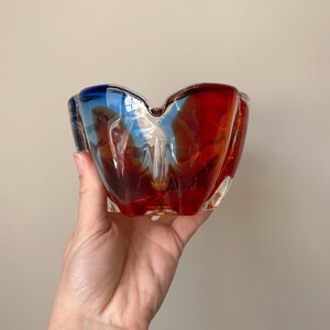May include: A red and blue glass ashtray with a wavy, organic shape.