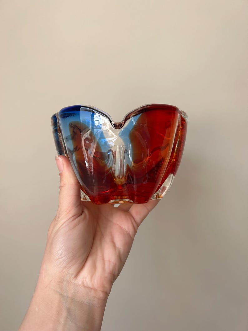 May include: A red and blue glass ashtray with a wavy, organic shape.