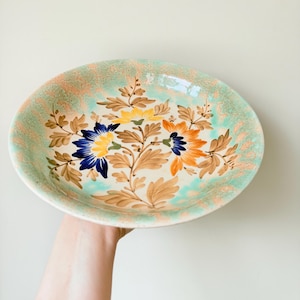 Peut inclure: Un bol de service en céramique vintage avec un motif floral. Le bol est recouvert d'un glaçage vert clair avec un motif floral brun et orange.