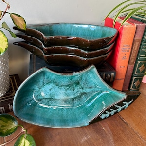 以下が含まれることがあります： ターコイズとブラウンのセラミック製の葉の形をしたボウルが3つ。ボウルは積み重ねられています。一番上のボウルが一番大きく、一番下のボウルが一番小さいです。ボウルは木製の表面の上に置かれています。