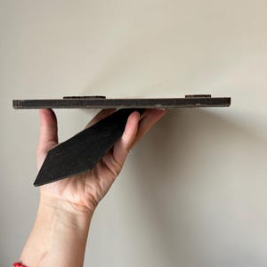 Puede incluir: Un marco de fotos de madera marr&oacute;n con un caballete negro. El marco tiene una superficie texturizada y est&aacute; listo para mostrar una foto o una obra de arte.
