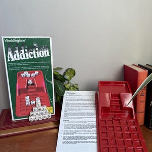 May include: A vintage board game called "Addiction" by Waddingtons. The box is green and white, with the game title in large letters. The game includes a red plastic game board, dice, and lettered tiles. The game is designed for solo or multiple players.