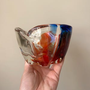 May include: A clear glass bowl with red, orange, and blue swirls. The bowl has a unique, irregular shape.