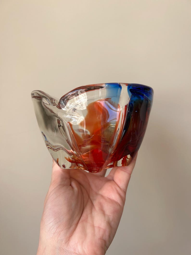 May include: A clear glass bowl with red, orange, and blue swirls. The bowl has a unique, irregular shape.