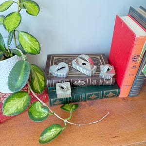 May include: Five silver cookie cutters in different shapes, including a heart, a rectangle, and a circle. The cutters are arranged on top of a stack of books.