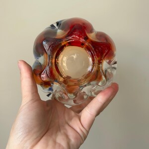 May include: A clear glass vase with a textured, wavy surface. The vase has a red, orange, and blue iridescent finish.