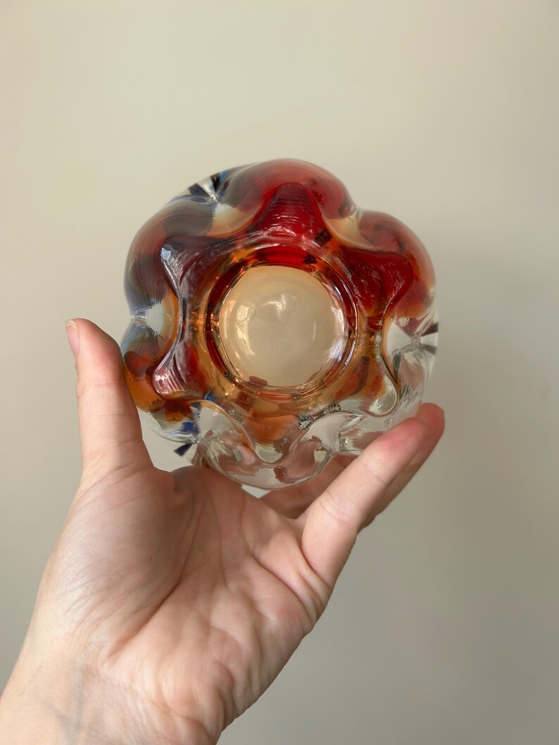 May include: A clear glass vase with a textured, wavy surface. The vase has a red, orange, and blue iridescent finish.