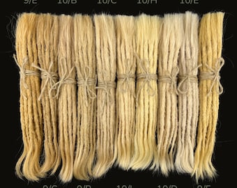 May include: A selection of blonde and light brown dreadlocks, each tied with twine, displayed against a black backdrop. The bundles are arranged in a row and labelled with codes like "9/E" and "10/B".