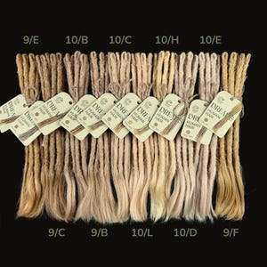 Może przedstawiać: Kolekcja przedłużeń do włosów ludzkich w różnych odcieniach blondu i brązu. Każdy pęczek jest oznaczony kodem koloru i etykietą z napisem "DREAM HUMAN HAIR". Przedłużenia są ułożone na czarnym tle.