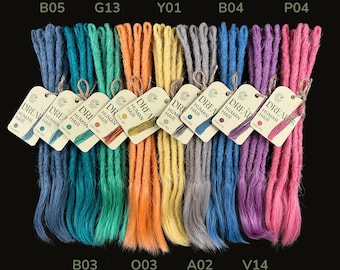 May include: A selection of vibrant dreadlocks in blue, green, orange, yellow, grey, purple, and pink. Each bundle has a tag that reads "DREAM HUMAN HAIR". The dreadlocks are displayed against a black backdrop.