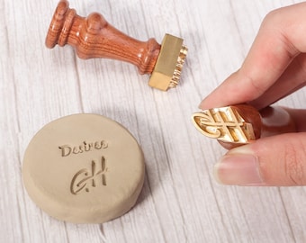 Puede incluir: Un sello de lacre con cabeza de latón pulido y mango de madera torneada, acompañado de un disco de arcilla redondo con el texto en relieve Desires y un monograma GH estilizado, que coincide con el diseño de la cabeza del sello de latón.