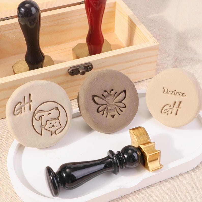 May include: Four wooden stamps with different designs. The stamps are in a wooden box with a brass latch. The designs include a bee, a cat and dog, and the letters GH. The stamps are used for wax sealing.