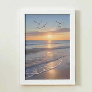 Può includere: Una stampa incorniciata con una serena scena di spiaggia al tramonto. L'immagine cattura il sole che tramonta sull'oceano, con dolci onde che lambiscono la riva. Uccelli silhouette volano nel cielo. La stampa è racchiusa in una cornice bianca.