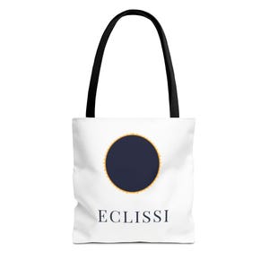 Könnte beinhalten: Weiße Tragetasche mit schwarzen Henkeln. Sie zeigt einen marineblauen Kreis mit goldenem Rand und das Wort "ECLISSI" in Marineblau darunter. Ideal zum Tragen von Gegenständen.