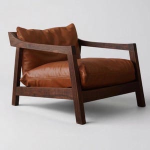 Op de afbeelding: Een moderne fauteuil met een donkerhouten frame en bruine leren kussens. De stoel heeft een vierkant ontwerp met een hoge rug en armleuningen. De zit- en rugkussens zijn warmbruin van kleur.