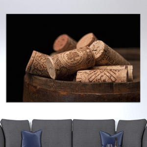 May include: Close-up of several used wine corks with printed designs, resting inside a weathered wooden barrel. The corks vary in size and shape, with visible text and illustrations. The background is a dark, blurred setting, emphasizing the corks.