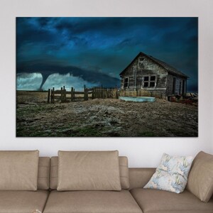 Puede incluir: Una impresión de paisaje dramático con un tornado formándose en un cielo oscuro y tormentoso. Una casa de madera vieja y desgastada y una valla están en primer plano. La obra de arte evoca una sensación de clima inminente y vida rural.