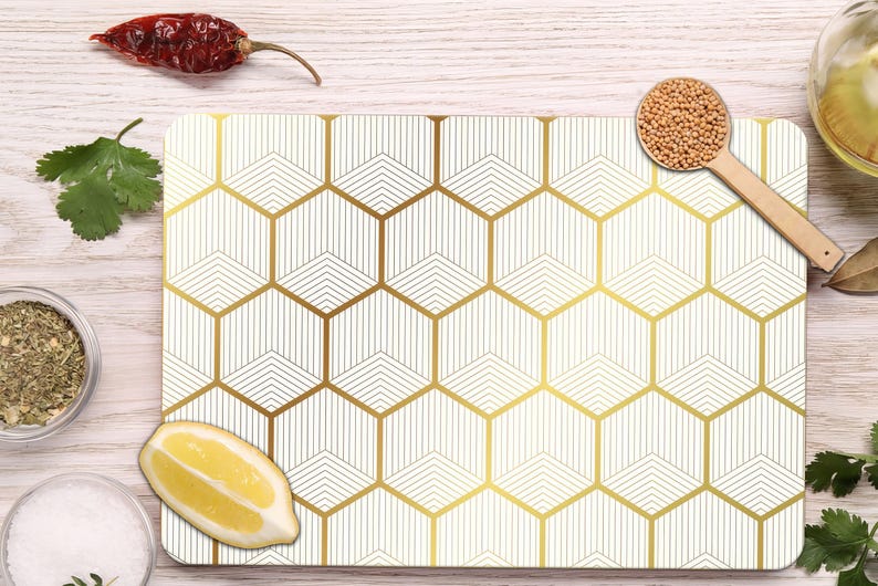 May include: A white and gold geometric pattern cutting board with a wooden spoon of mustard seeds, a red chili pepper, and a lemon wedge. Other ingredients include herbs and spices.