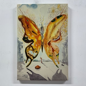 May include: A canvas print of a surrealist painting featuring a butterfly with wings in shades of yellow and brown. The artwork includes a landscape with architectural elements, a figure, and the artist's signature.