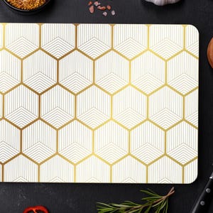 May include: Rectangular cutting board with a geometric gold and white pattern. The board is surrounded by ingredients like spices, herbs, and a knife, suggesting a culinary theme. The design features a repeating hexagon pattern.