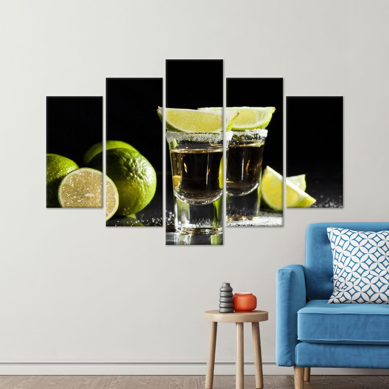 May include: Two clear shot glasses filled with a golden liquid, garnished with lime wedges and a rim of sugar. The glasses are on a black surface with lime wedges scattered around them.