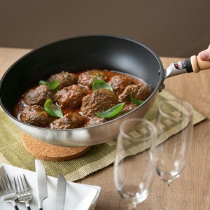 Pu&ograve; includere: Una padella d'argento con manico di legno, piena di salsa rossa e cibo simile a polpette ricoperto di erbe verdi.