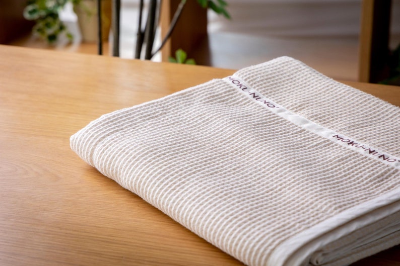 May include: A white waffle weave towel with the text "MOKI-NUNO" printed in brown on the fabric.