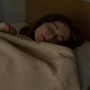 May include: A person sleeping under a beige waffle weave blanket with the text "MONO MONO" embroidered on it.