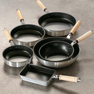 Pu&ograve; includere: Un set di cinque padelle in ghisa nera con manici in legno. Le padelle sono di diverse dimensioni e forme, tra cui una padella rettangolare.