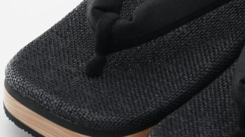 May include: Black woven fabric sandals with a wooden sole. The sandals have a simple design and are made of a durable material.