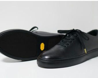 May include: A pair of black leather low-top sneakers with white soles. The shoes have a lace-up closure and a gold accent on the side.