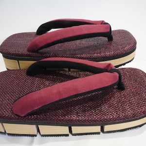 Könnte beinhalten: Ein Paar burgunderfarbene japanische Sandalen mit schwarzen Riemen und einer Holzplattformsohle.