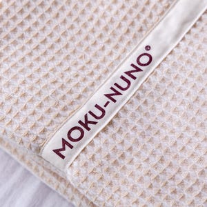 May include: A close-up of a beige waffle weave towel with a white label that says "MOKU-NUNO" in burgundy lettering.