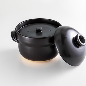 Puede incluir: Una olla de cerámica negra con tapa, la tapa está ligeramente entreabierta. La olla tiene dos asas y una pequeña perilla en la tapa.