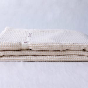 May include: A folded waffle weave cotton throw blanket in a cream color. The blanket has a small label with the text "Made in China" on it.