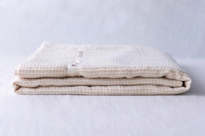 May include: A folded waffle weave cotton throw blanket in a cream color. The blanket has a small label with the text "Made in China" on it.