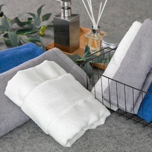 May include: A set of towels in various colors, including blue, gray, and white, are folded and stacked on a gray surface. The towels are arranged in a wire basket.