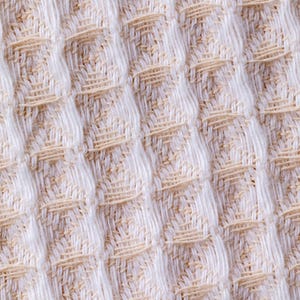 May include: Close-up of a white and beige waffle weave fabric. The fabric has a textured, raised pattern.