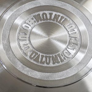 Pu&ograve; includere: Primo piano di un disco di metallo argentato con le parole "OPTIMUM QUALITY" e "CAST IRON" incise attorno al centro.