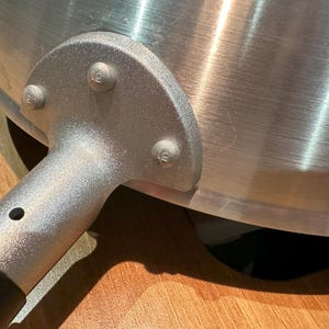 Pu&ograve; includere: Primo piano di un manico di wok in metallo argentato con quattro rivetti. Il manico &egrave; attaccato al wok con un pezzo di metallo curvo.