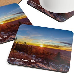 Peut inclure: Quatre sous-verres carrés avec une image de coucher de soleil panoramique de Spruce Knob, WV. Les sous-verres sont en liège et ont une bordure noire. Une tasse blanche avec du café est posée sur l'un des sous-verres.