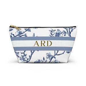 Front view of a personalized blue toile accessory pouch with horizontal stripes and gold monogram initials.