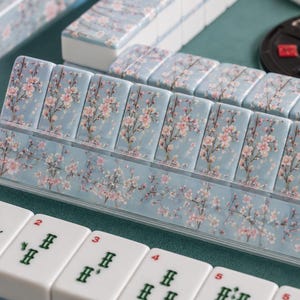 Close-up of cherry blossom Mahjong tiles showcasing the soft blue background with elegant pink cherry blossom branches and detailed American Mahjong tile faces.