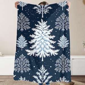 May include: A navy blue blanket with a repeating pattern of white winter trees and stars. The central tree is a detailed evergreen. The blanket is held up, showing the design and soft texture, perfect for the winter season.